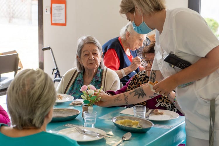 Photo représentant une patiente à table et une professionnelle de santé positionnant un bouquet de fleurs dans un vase situé devant la patiente et sur la table de la clinique des minimes